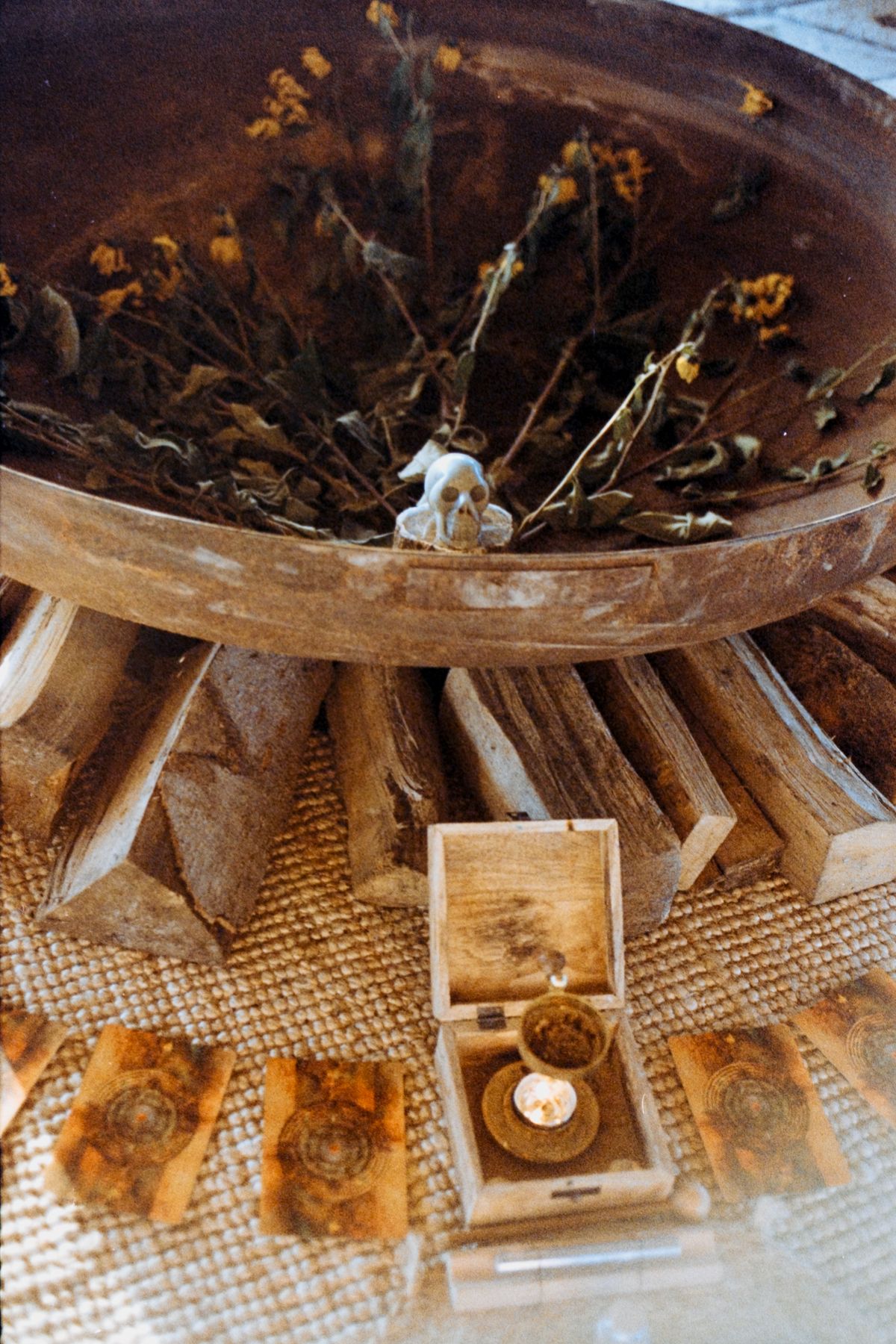 A fire bowl filled with dried flowers above stacked wood and a candle.