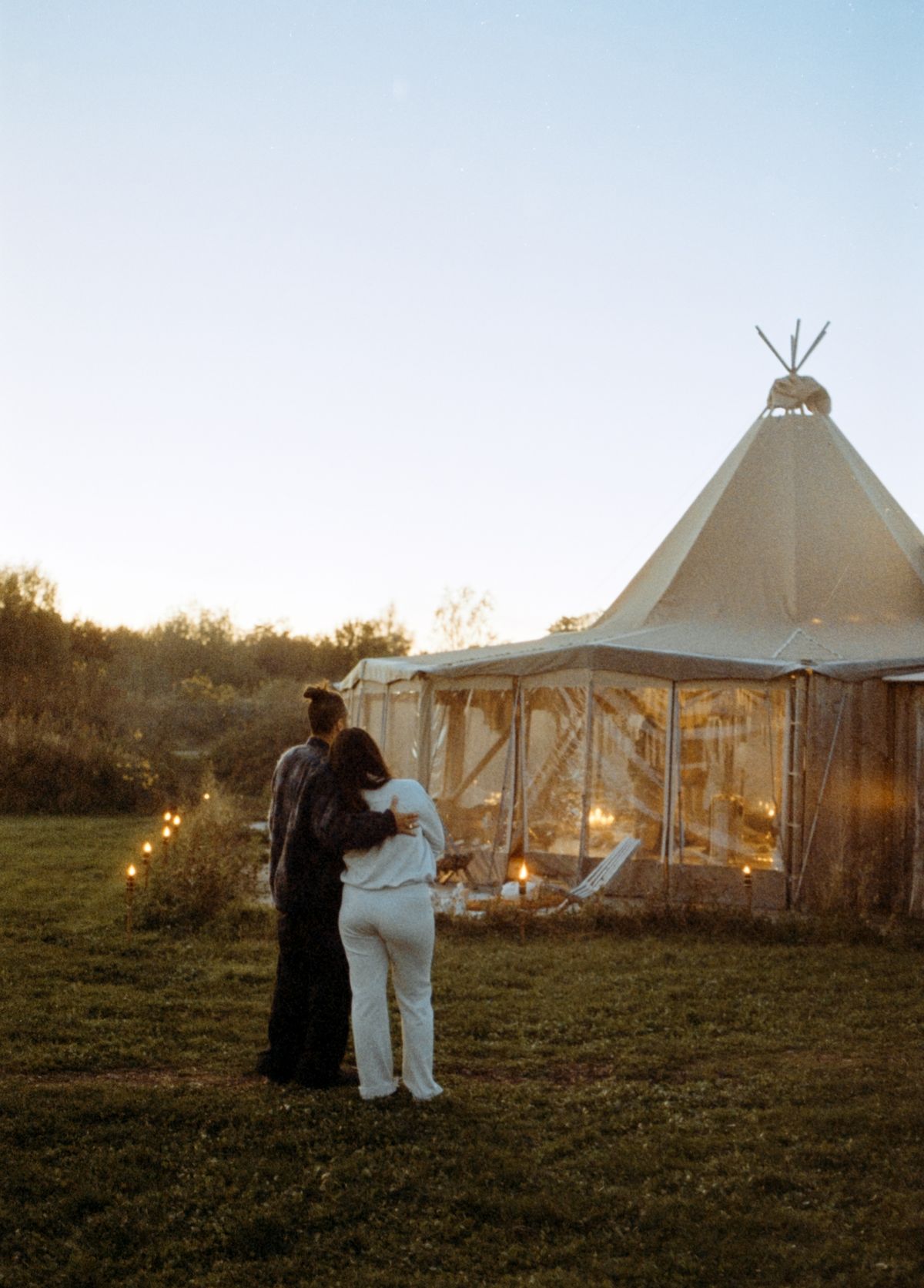 Two people embracing by a tipi at dusk.